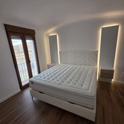 Cama tapizada con paneles de led y mesitas de colgar